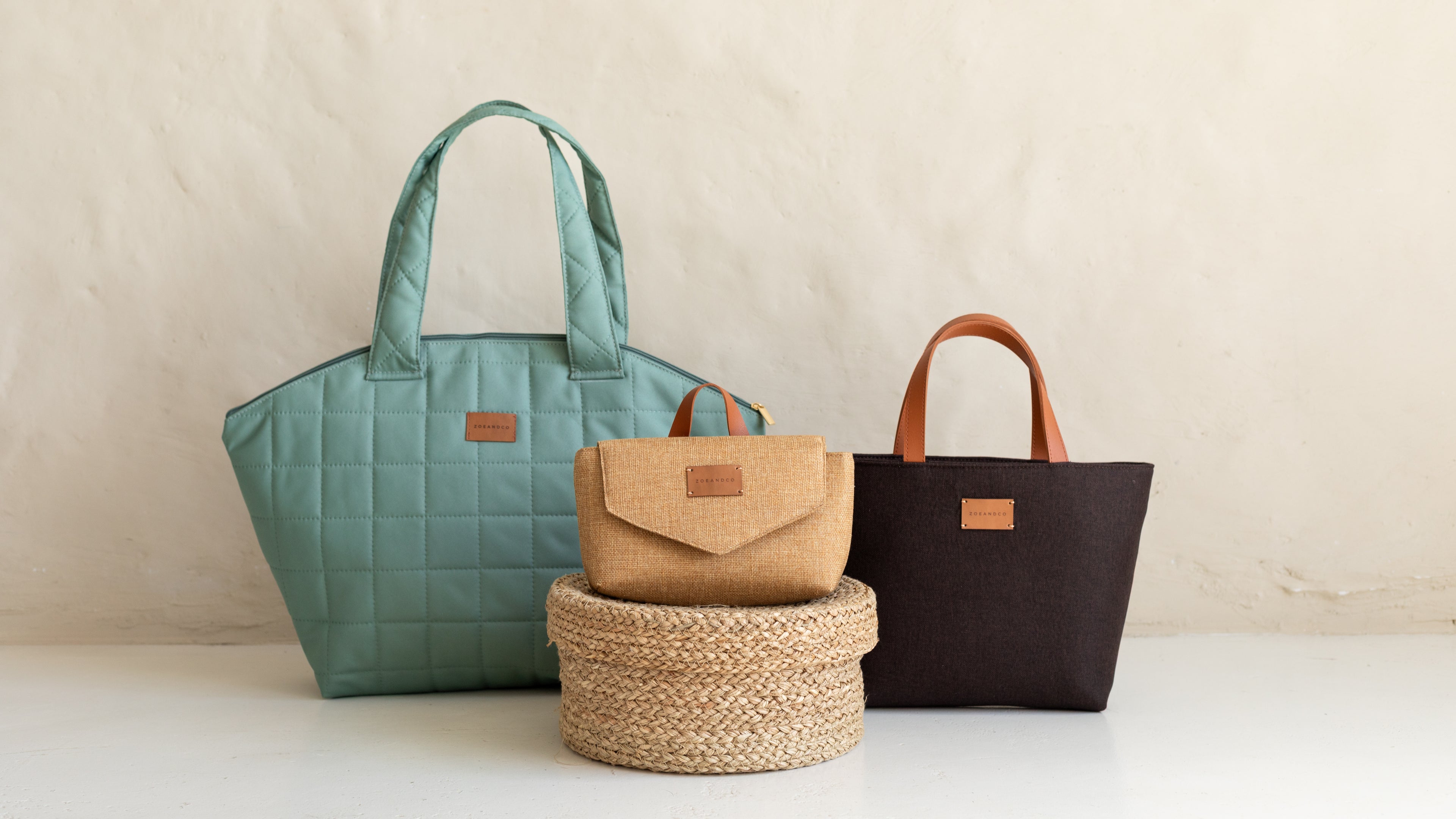 Three bags including a teal quilted handbag, a brown leather bag, and a black woven basket on a light background.